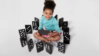 Mädchen sitzt in einem Kreis aus großen Dominosteinen