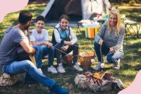 Eine Familie im Zelturlaub grillt Marshmallows am Lagerfeuer