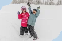 Zwei Kinder recken die Arme nach oben im Schnee und lachen