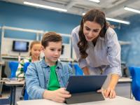 Ein Schüler arbeitet an einem Tablet und eine Lehrerin erklärt ihm etwas.